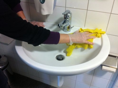 Frau reinigt ein Waschbecken im Rahmen der gemeinnützigen Arbeit. 