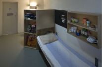 Bett und Gestelle mit privaten Gegenständen in einer Zelle